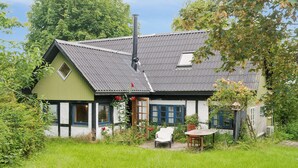 A house with a sloped roof, a chimney, and a small garden area with a chair and table. - Unique private idyll (Vesterborg)