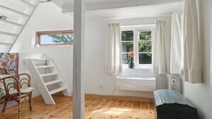A room with a wooden floor, a window with curtains, a white radiator, a white chair, and a staircase. - Unique private idyll (Vesterborg)