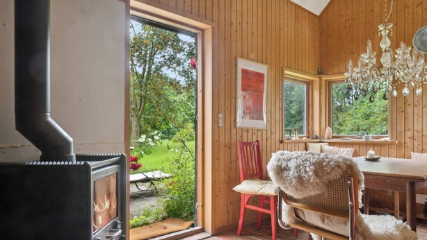 A wooden interior with a fireplace, a dining area, and a view of a garden. - Unique private idyll (Vesterborg)