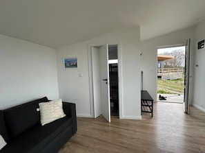 Une piÚce avec un canapé noir, une porte blanche donnant sur un balcon et un plancher en bois.