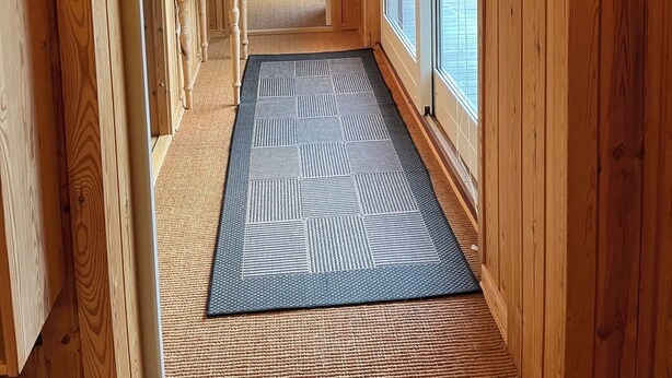 A wooden hallway with a rug, a table with a lamp, and a chair.