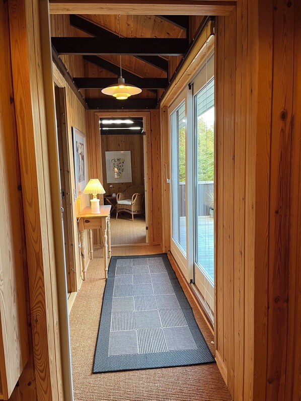 A wooden hallway with a rug, a table with a lamp, and a chair.