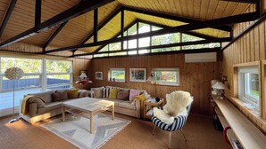 A wooden interior with a high ceiling, a sofa, a chair, a coffee table, and a window.