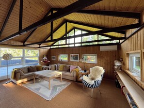 A wooden interior with a high ceiling, a sofa, a chair, a coffee table, and a window.