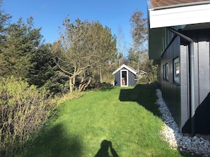 A small shed in a grassy yard with trees in the background.