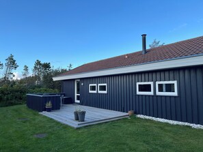 A modern house with a dark exterior, a red-tiled roof, and a wooden deck.