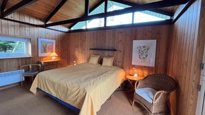A wooden-paneled room with a bed, two bedside tables with lamps, a chair, and a radiator.