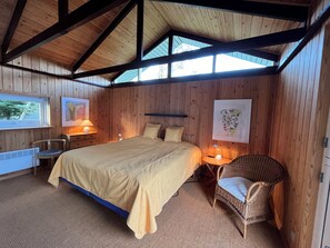 A wooden-paneled room with a bed, two bedside tables with lamps, a chair, and a radiator.