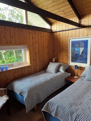 A cabin with two beds, a window, a framed picture, and a lamp.