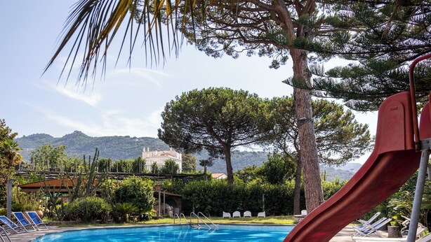 A swimming pool with a red slide, surrounded by lounge chairs and trees. - Gargiulo Suites (Piano di Sorrento)