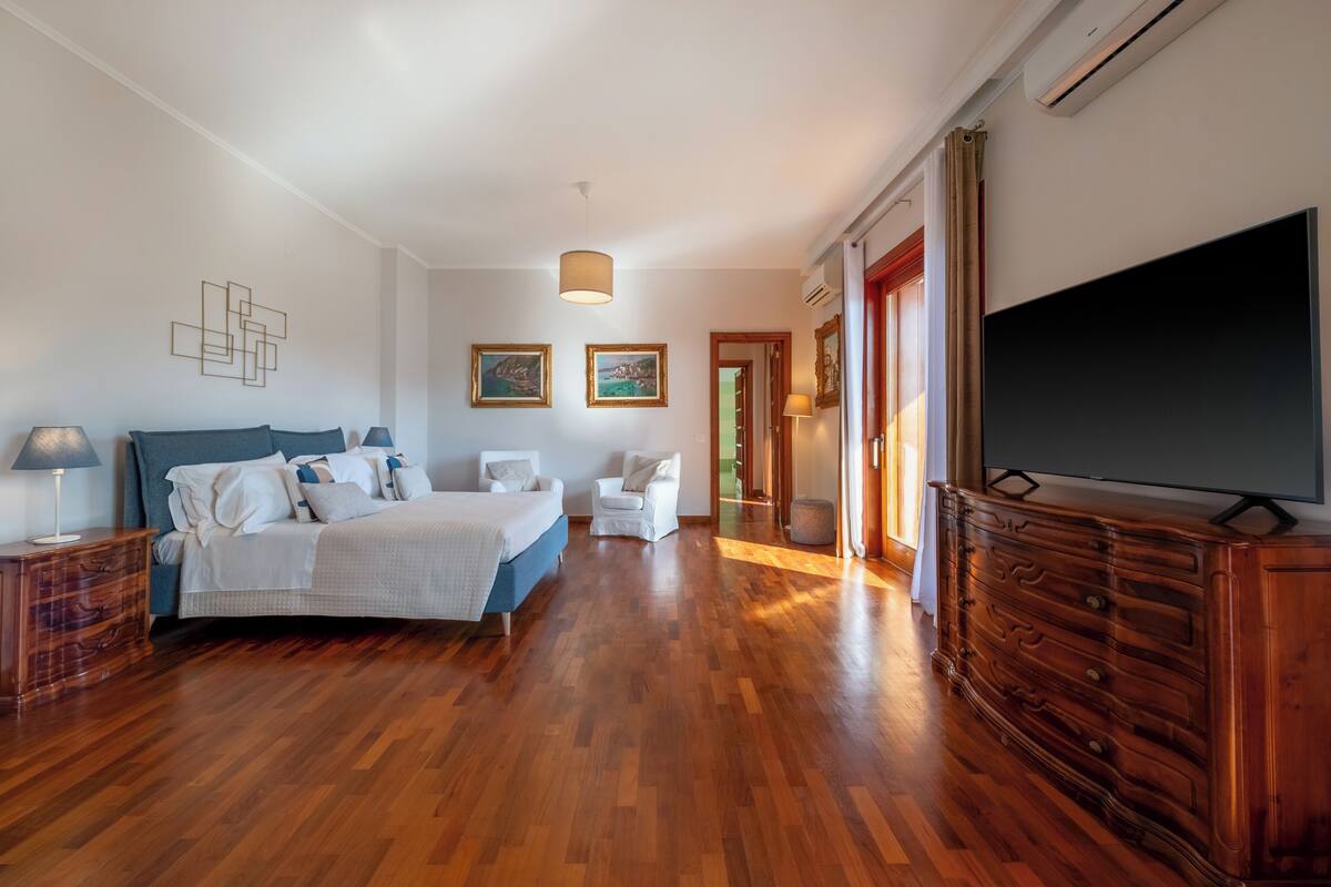 Um quarto espaçoso com uma cama grande, penteadeira, televisão e uma cadeira.