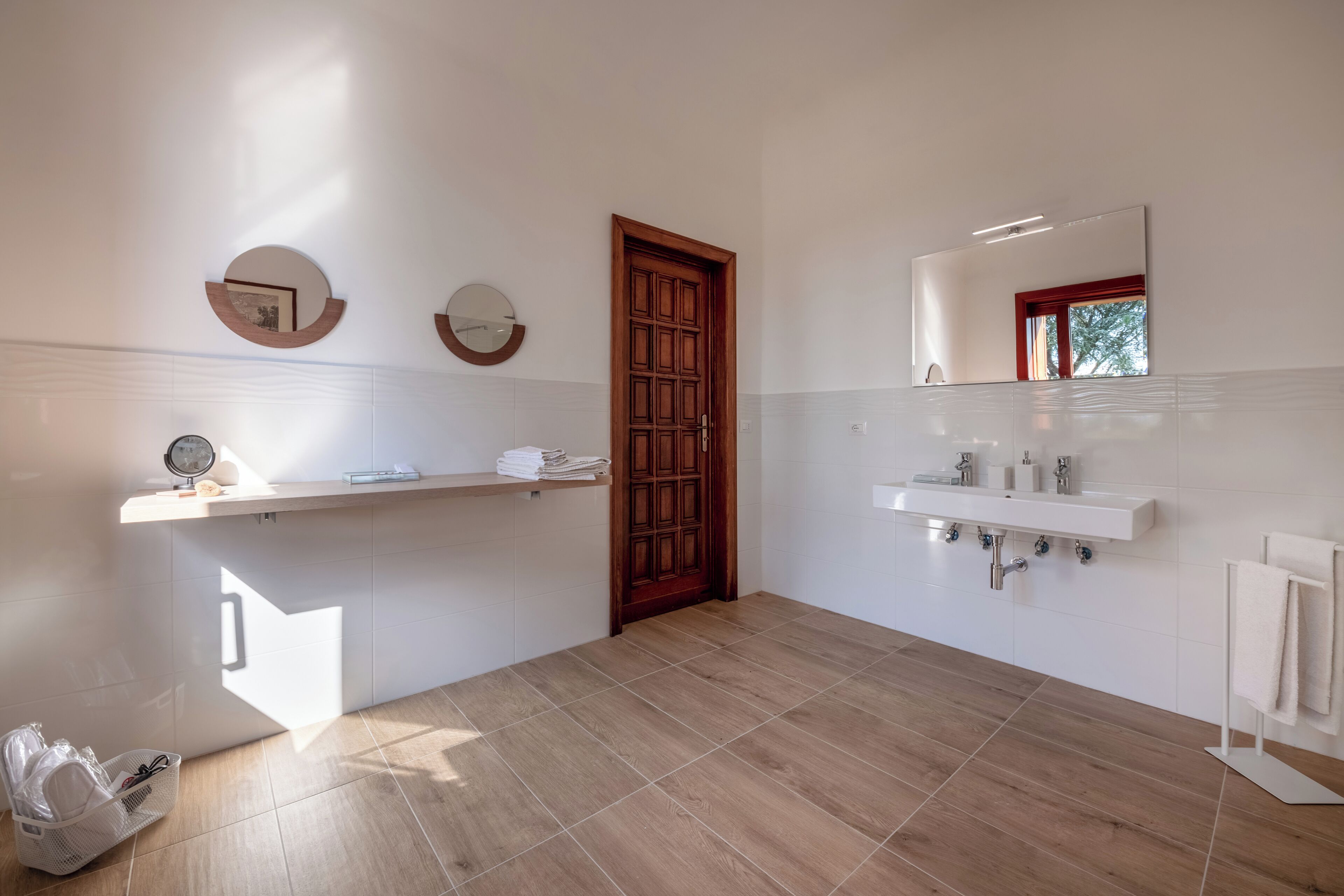 A modern bathroom with a wooden door, a large mirror, a white sink, and a towel rack.
