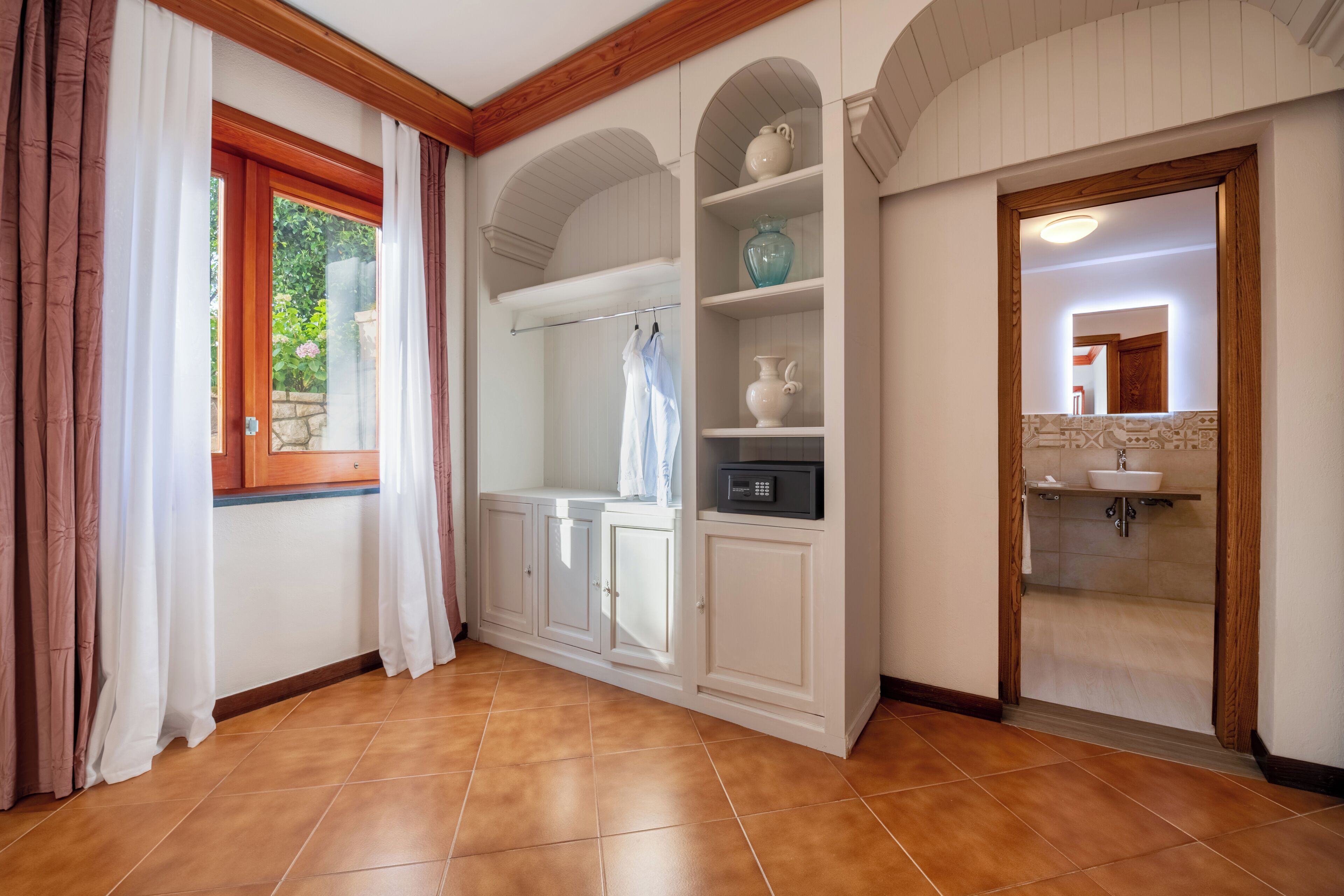 A room with a wooden floor, white cabinets, a built-in microwave, and a window with curtains.
