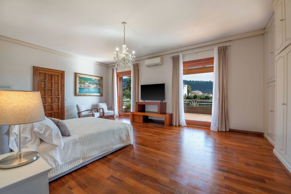 Um quarto espaçoso com piso de madeira, uma cama, uma televisão, uma escrivaninha e uma cadeira.