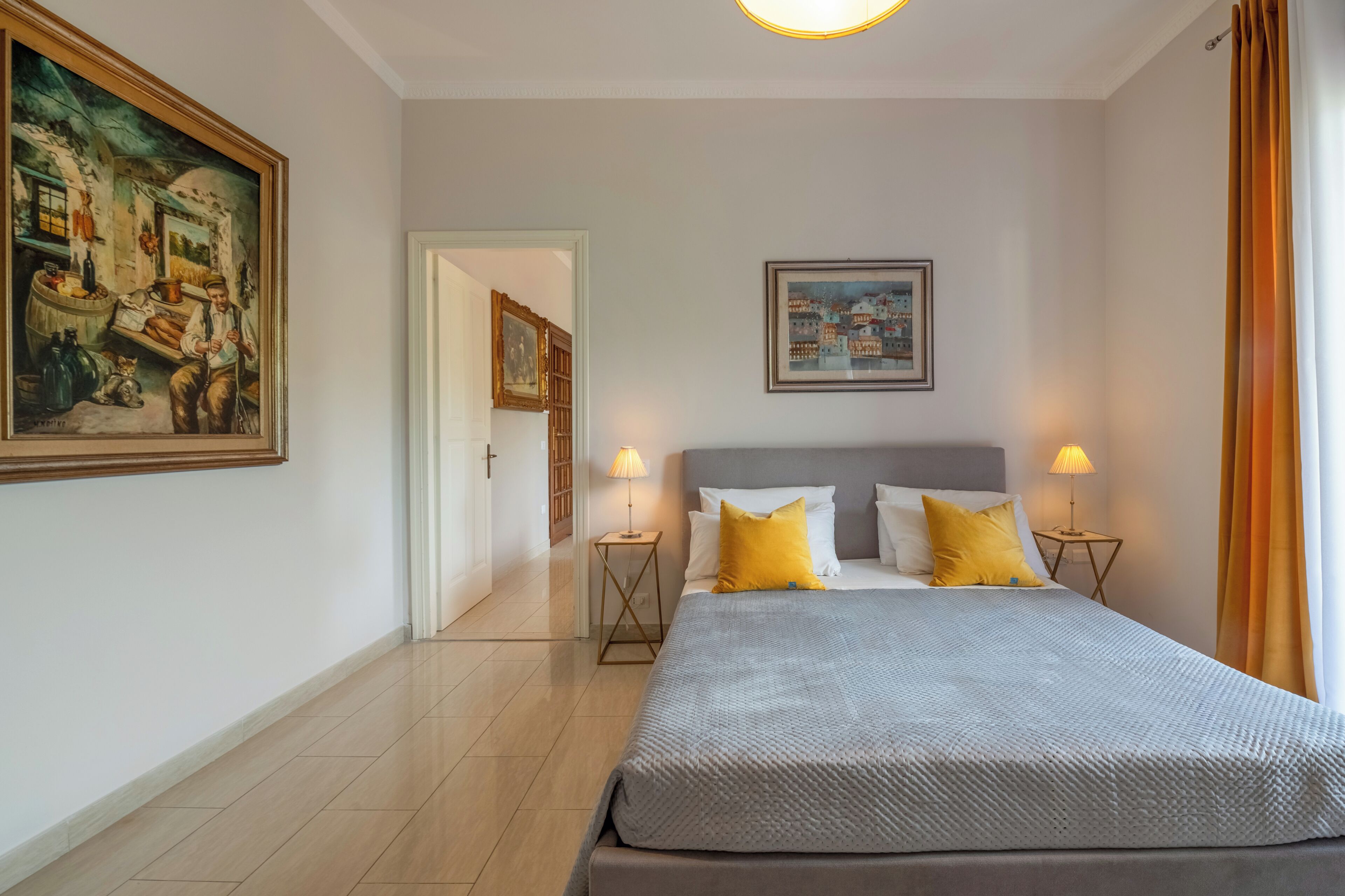 Ein Hotelzimmer mit einem großen Bett, zwei Nachttischen mit Lampen, einem Gemälde an der Wand und einer Tür zu einem weiteren Raum.