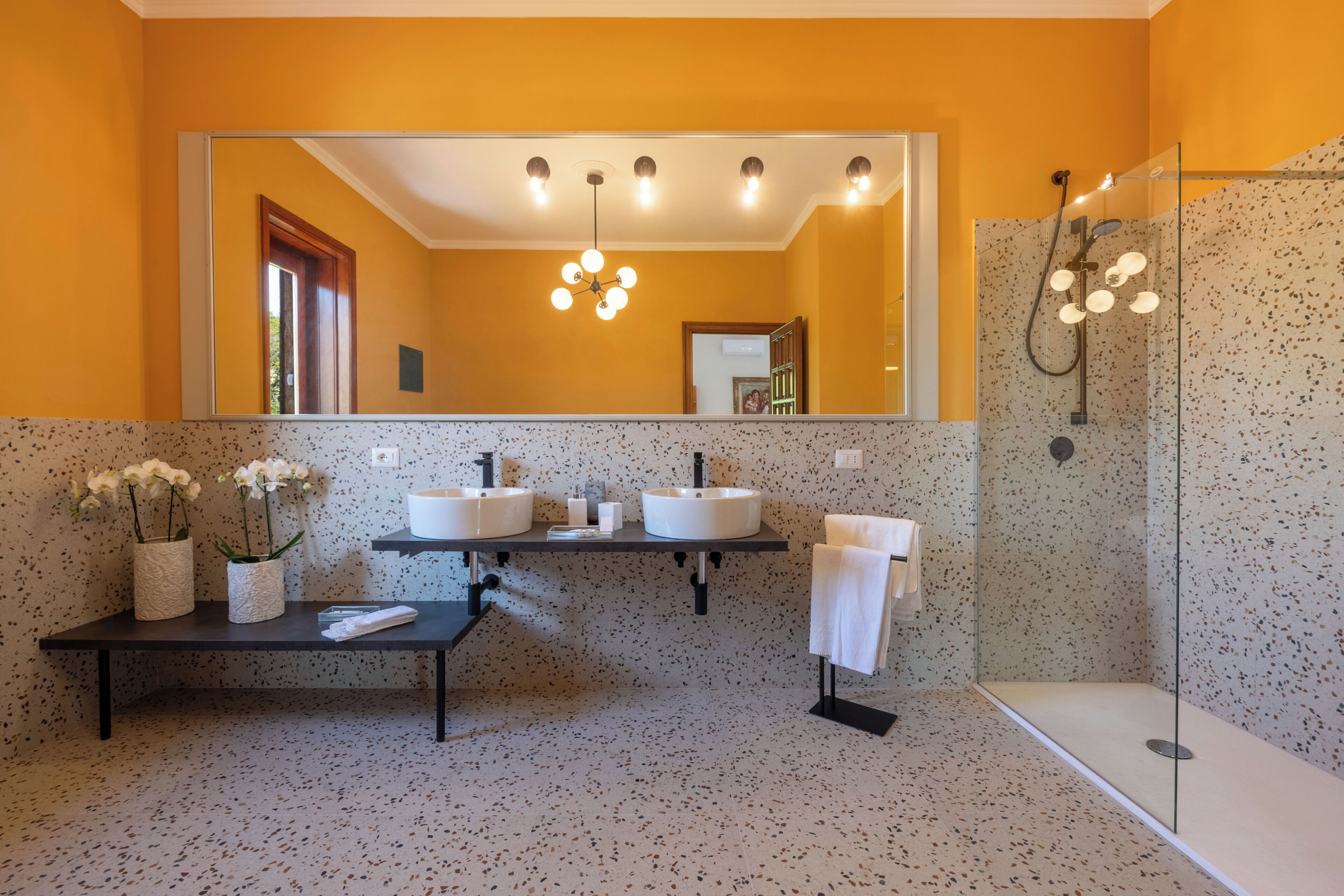 Uma casa de banho moderna com duas pias, um espelho grande, chuveiro e um banco com toalhas.