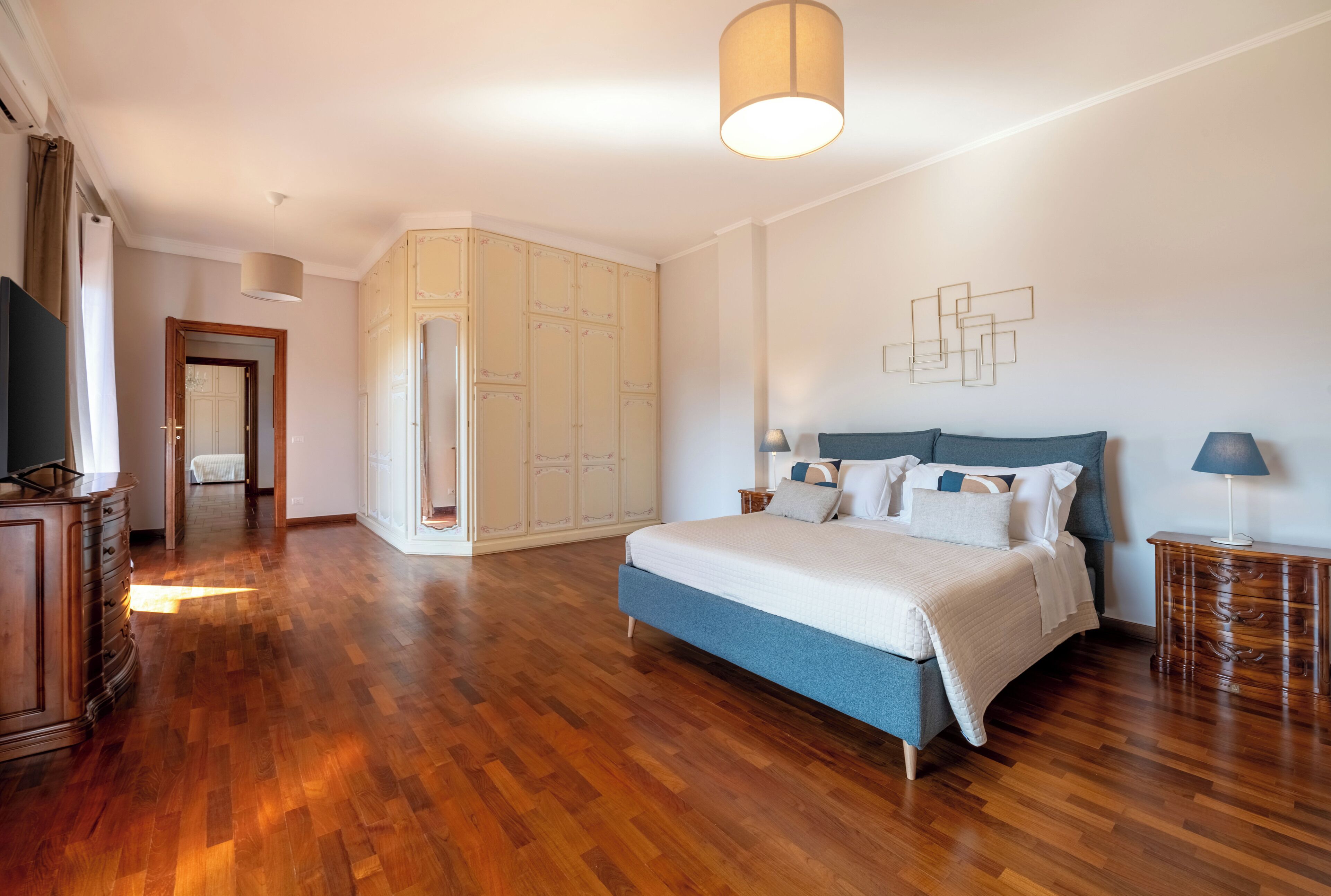 A bedroom with a large bed, wooden flooring, a wardrobe, and a television.