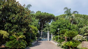 A paved pathway leading to a gated entrance surrounded by lush greenery and trees. - Gargiulo Suites (Piano di Sorrento)