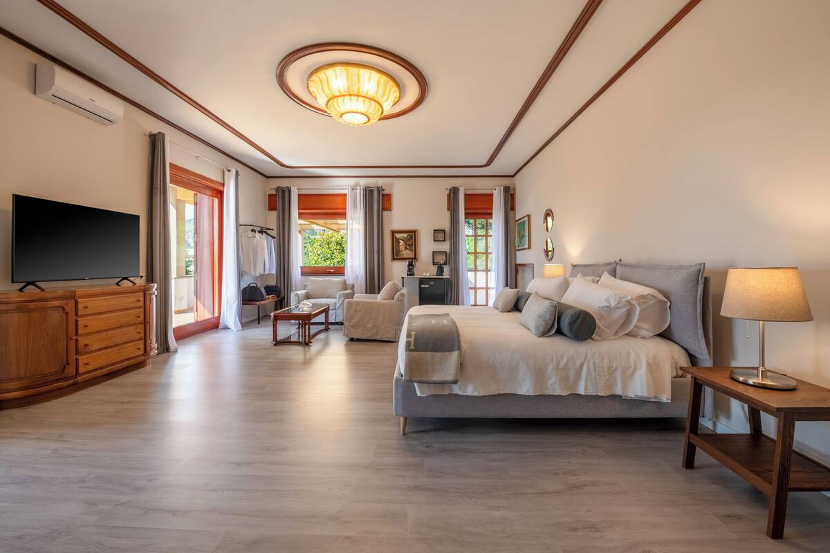 Um quarto espaçoso com uma cama grande, televisão, c ômoda de madeira e um candelabro.