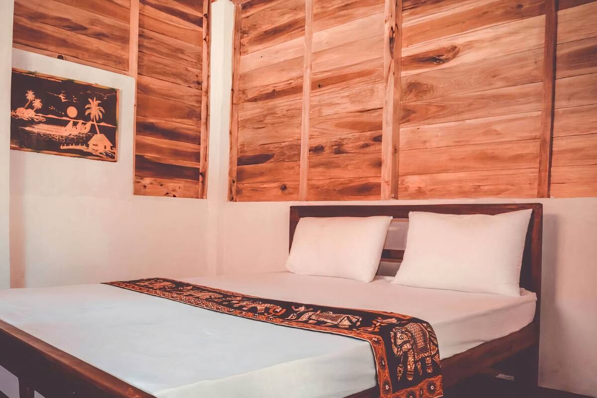 Un dormitorio con cabecera de madera, cama con sábanas blancas y una manta decorativa.