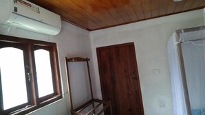 A room with a wooden ceiling, a window with a wooden frame, a white air conditioning unit, a wooden door, and a bed with a white bedspread. - Ocean View Beach Resort (Kudawa)