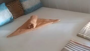 A neatly made bed with a rolled towel, patterned pillows, and striped bedspreads.