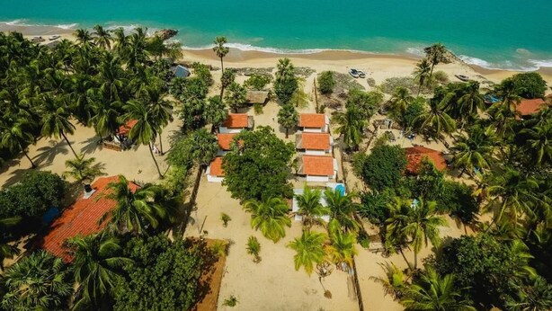 An aerial view of a beach resort with multiple bungalow-style buildings, palm trees, and a clear view of the ocean. - Ocean View Beach Resort (Kudawa)
