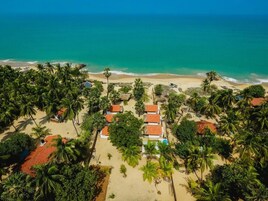 Vista aérea de um resort à beira-mar, com várias construções em estilo de bangalô, palmeiras e uma visão desobstruída do oceano.
