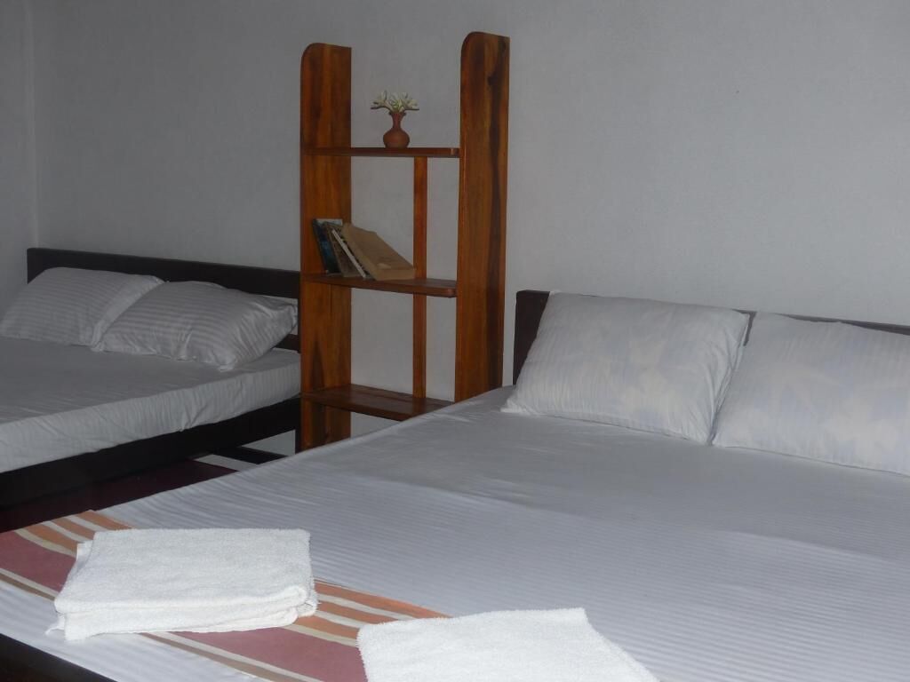 Habitación de hotel con dos camas, un estante de madera con una planta pequeña y una toalla doblada con cuidado sobre la cama.