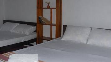 Habitación de hotel con dos camas, un estante de madera con una planta pequeña y una toalla doblada con cuidado sobre la cama.