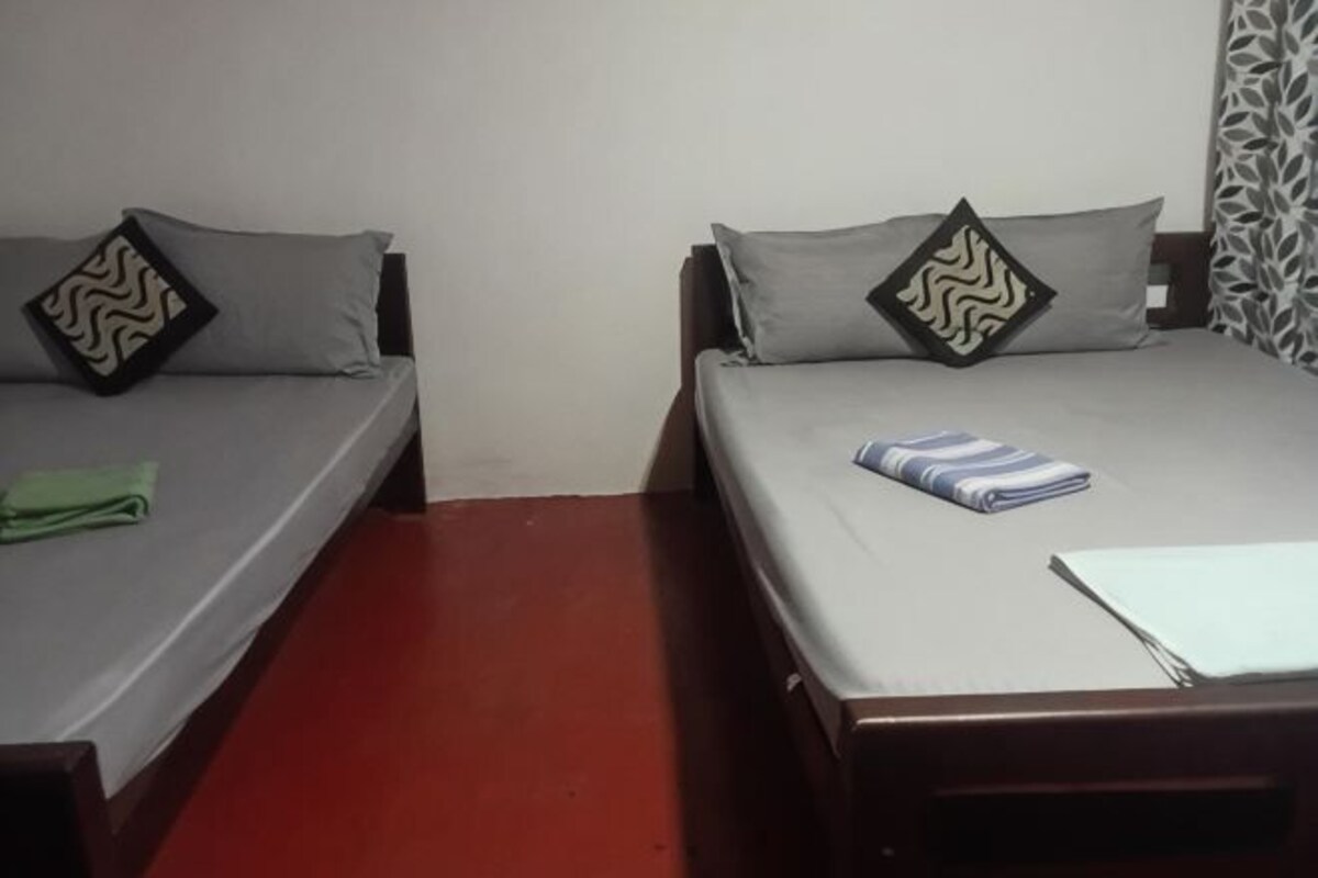 Two single beds with grey bedding and patterned pillows, a red floor, and a patterned curtain.