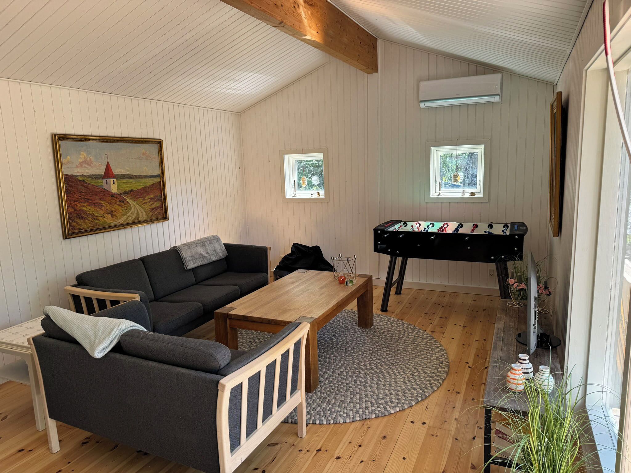 A cozy room with a sofa, a wooden coffee table, a foosball table, and a painting on the wall.