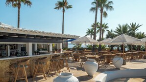 A bar area with wooden stools, large white vases, and outdoor tables and chairs.