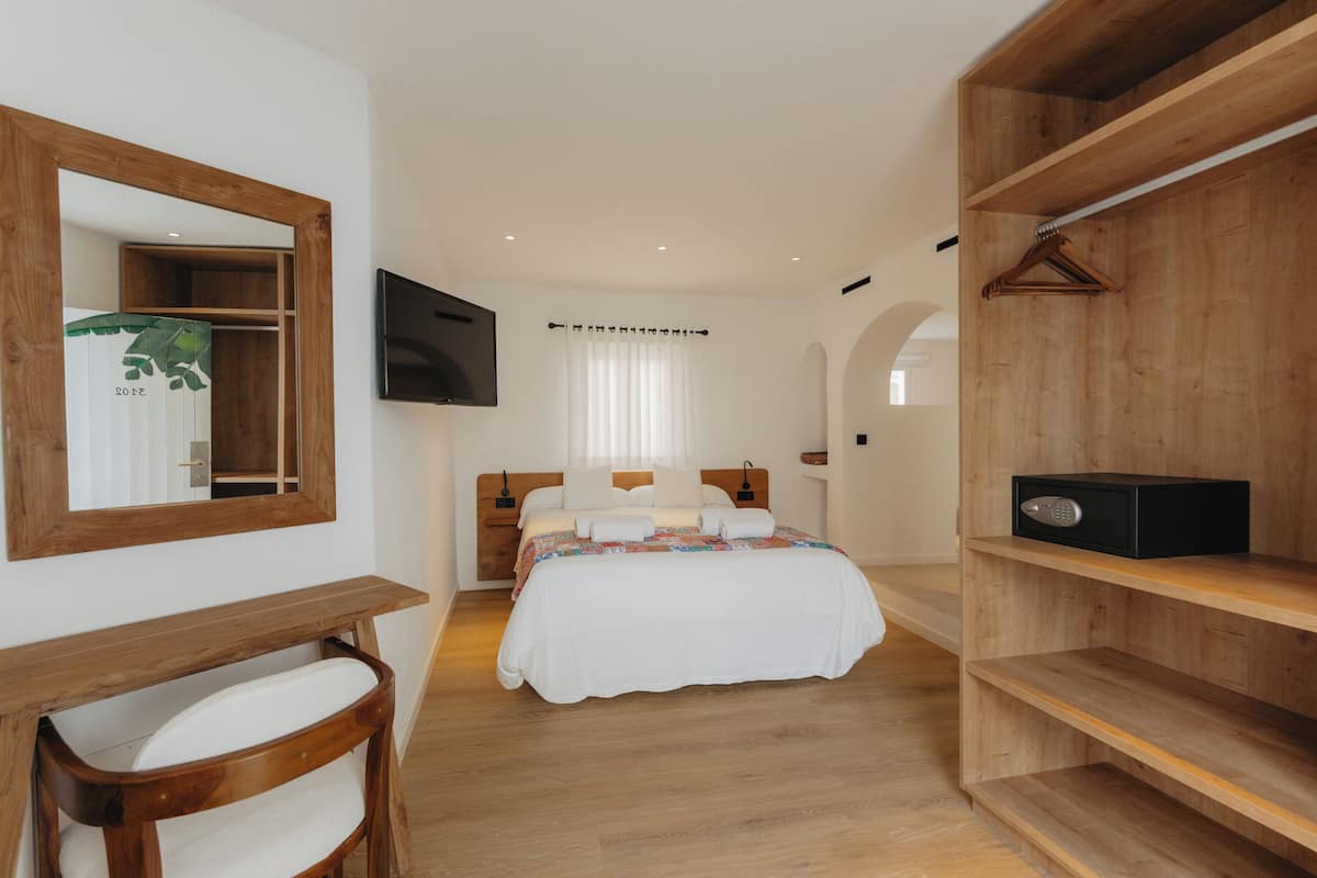 A bedroom with a bed, a wooden desk, a chair, a TV mounted on the wall, and a wardrobe.
