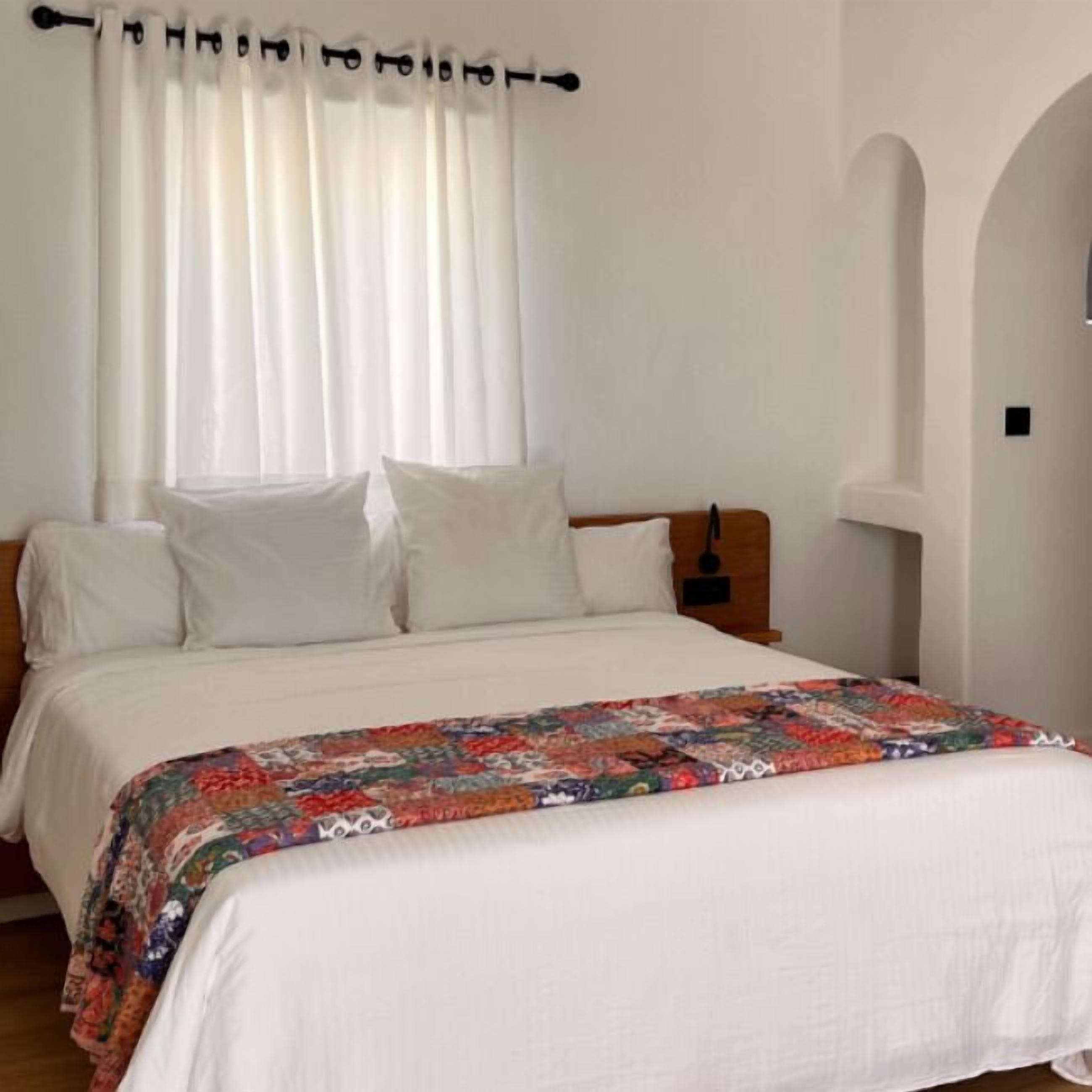 Un dormitorio con cama, cortinas blancas y colcha colorida.