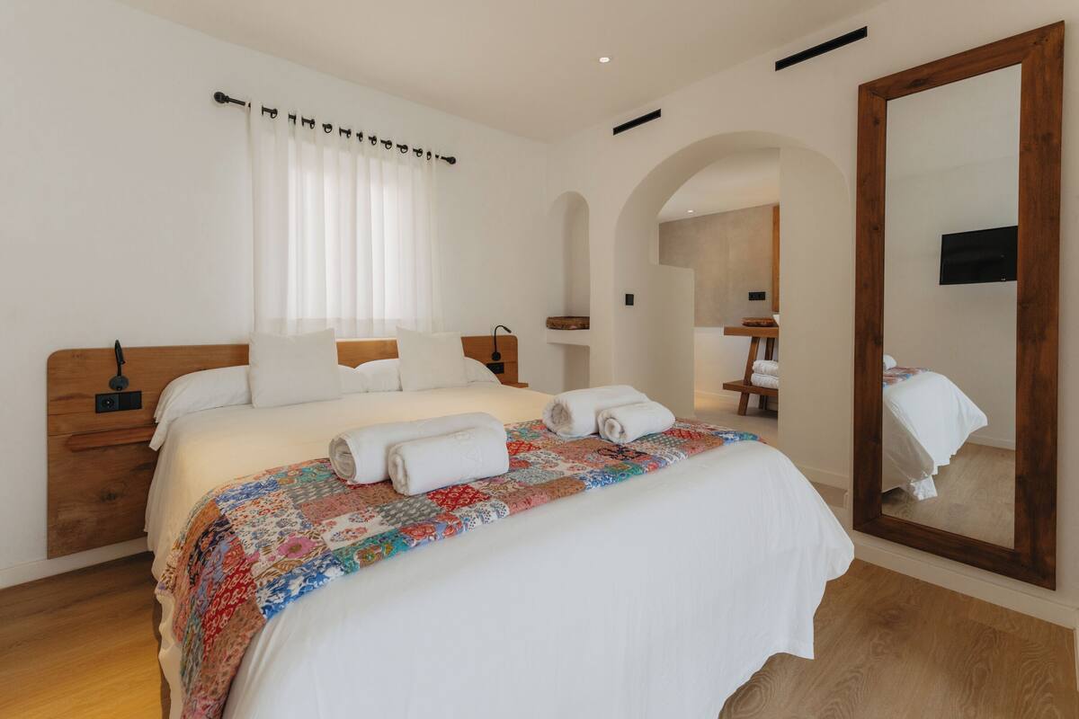 A neatly made bed with a colorful quilt, a large mirror, and a wooden headboard.