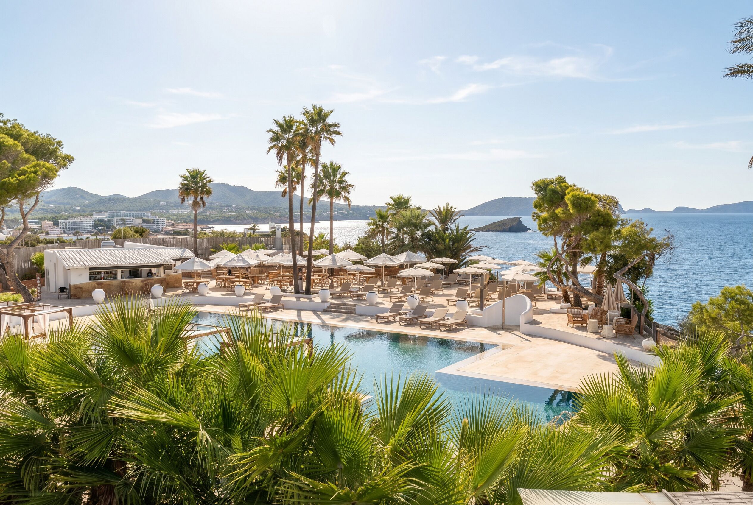 A resort with a pool, sun loungers, umbrellas, and a view of the sea.