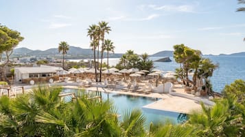 A resort with a pool, sun loungers, umbrellas, and a view of the sea.