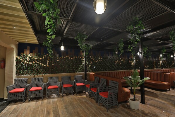 Een hal met rieten stoelen en banken, een houten vloer en een decoratieve wand met planten.