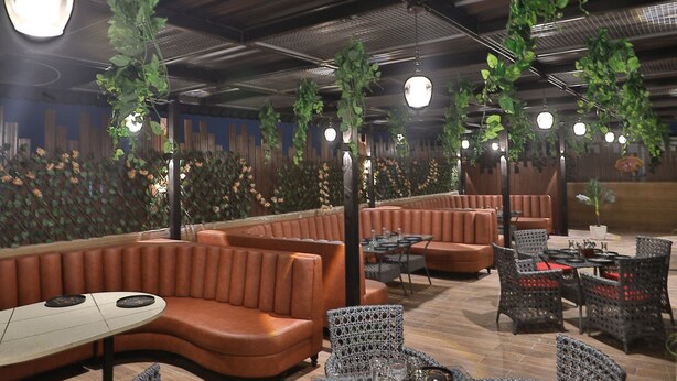 A restaurant with wicker furniture, cushioned seating, and hanging plants.