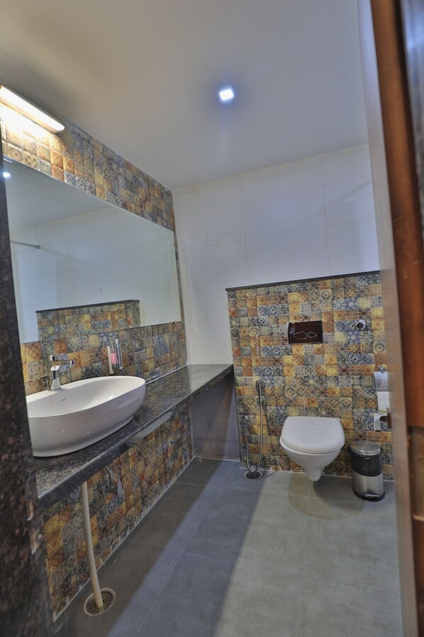 A bathroom with a sink, mirror, toilet, and patterned tiles.