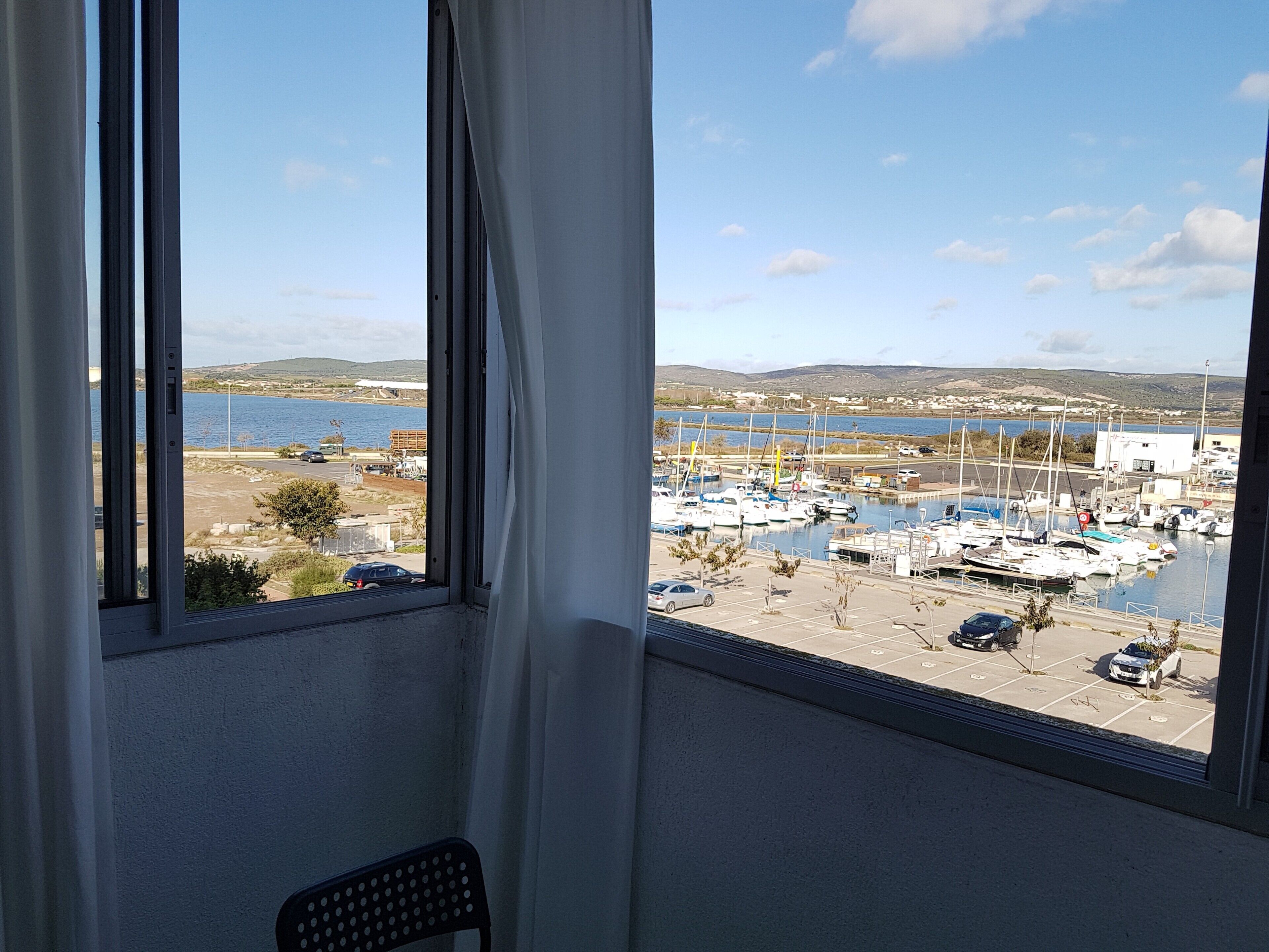 Une vue depuis une chambre dotée d’une grande fenêtre donnant sur une marina, avec des bateaux et une étendue d’eau.