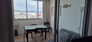 Una habitación con una mesa y sillas de comedor, un sofá, vistas a un puerto deportivo con barcos y una decoración de peces en la pared.
