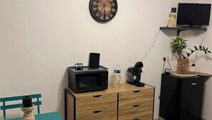 A compact room with a wooden desk, a microwave, a coffee maker, a clock, a television, and a small cabinet. - 1 Bedroom Apartment in Beauvoisin (Beauvoisin)