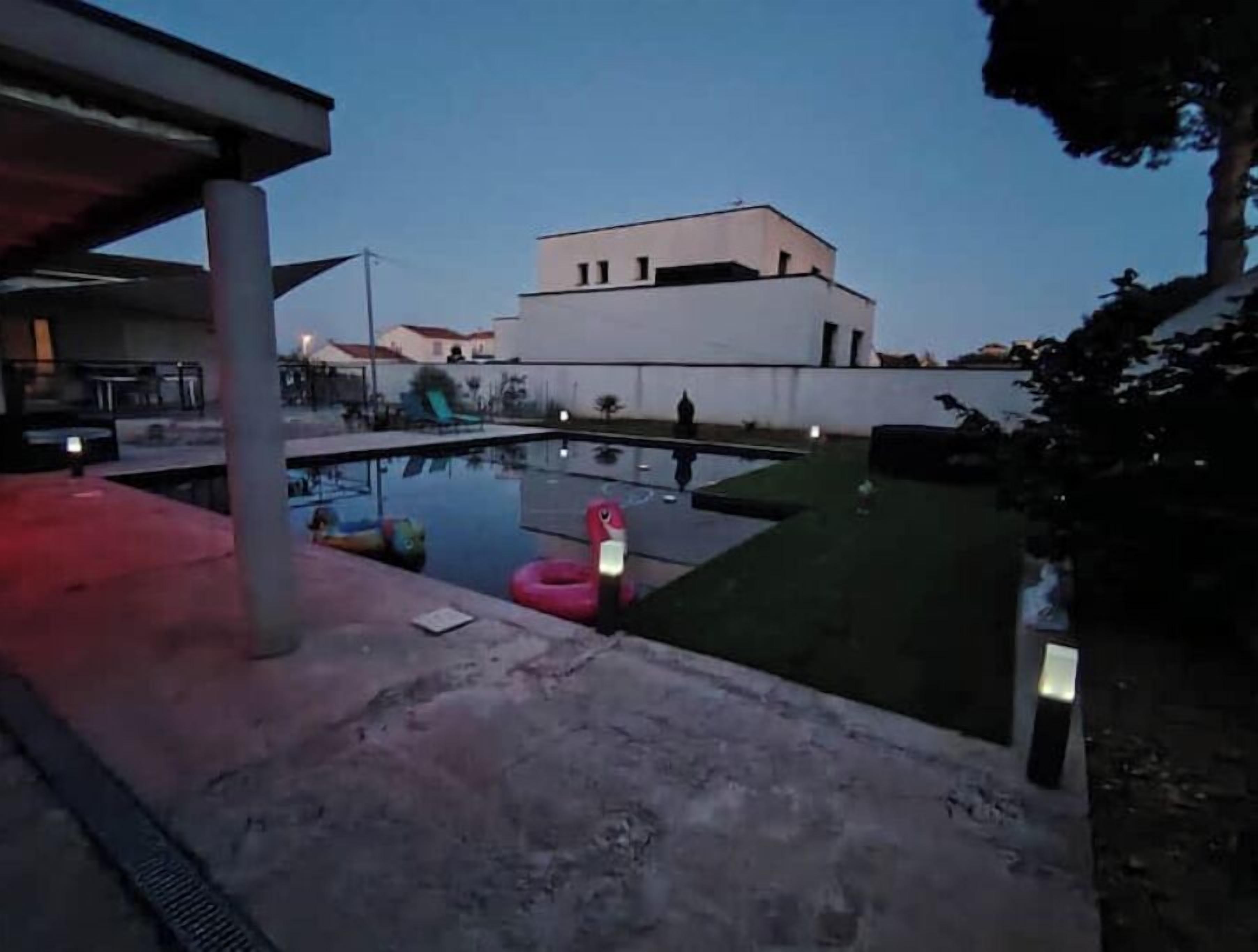 A swimming pool with a slide and inflatable toys, surrounded by a concrete deck and a building in the background.