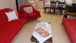 Una sala de estar con un sofá rojo, una mesa de comedor preparada con vasos y pastel, y una cocina al fondo.