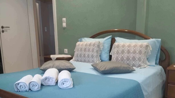 Una cama bien hecha con ropa de cama azul y almohadas blancas, un cabecero de madera y toallas enrolladas sobre la cama.