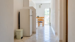 A narrow hallway with a refrigerator and a trash bin on the left, leading to a dining area with a table and chairs. - Apartments Katica's Place (Blato)