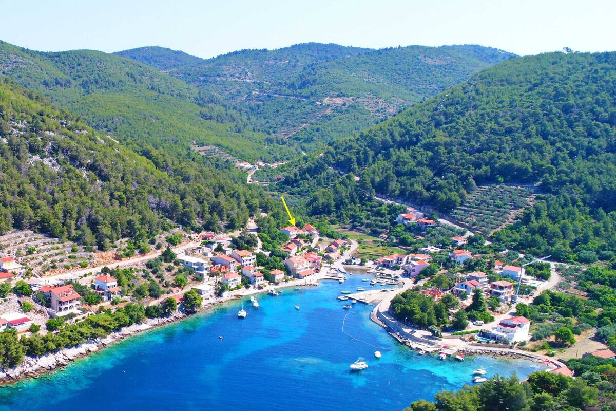 A coastal town with houses along the waterfront, boats docked, and a hilly backdrop.