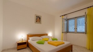 A neatly made bed with pillows, a bedside table with a lamp, and a window with curtains. - Apartments Katica's Place (Blato)
